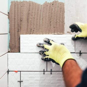 industrial construction worker installing small ceramic tiles on bathroom walls and applying mortar with trowel